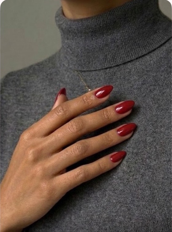 A hand resting on a grey knit jumper with glossy classic red almond nails.